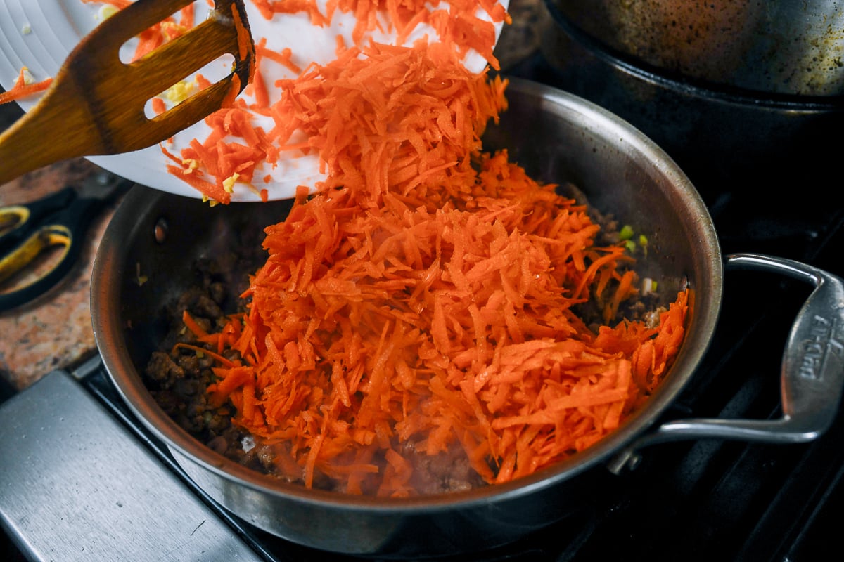 adding grated carrot to pork in skillet