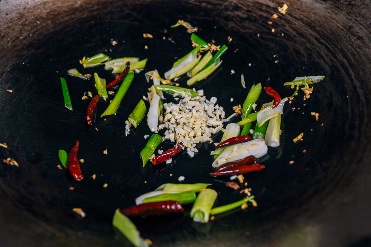 adding scallions to wok with oil, garlic, and ginger